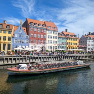 Vibrant canalside view of Nyhavn's colorful historic houses and tourist boats in Copenhagen, Denmark.